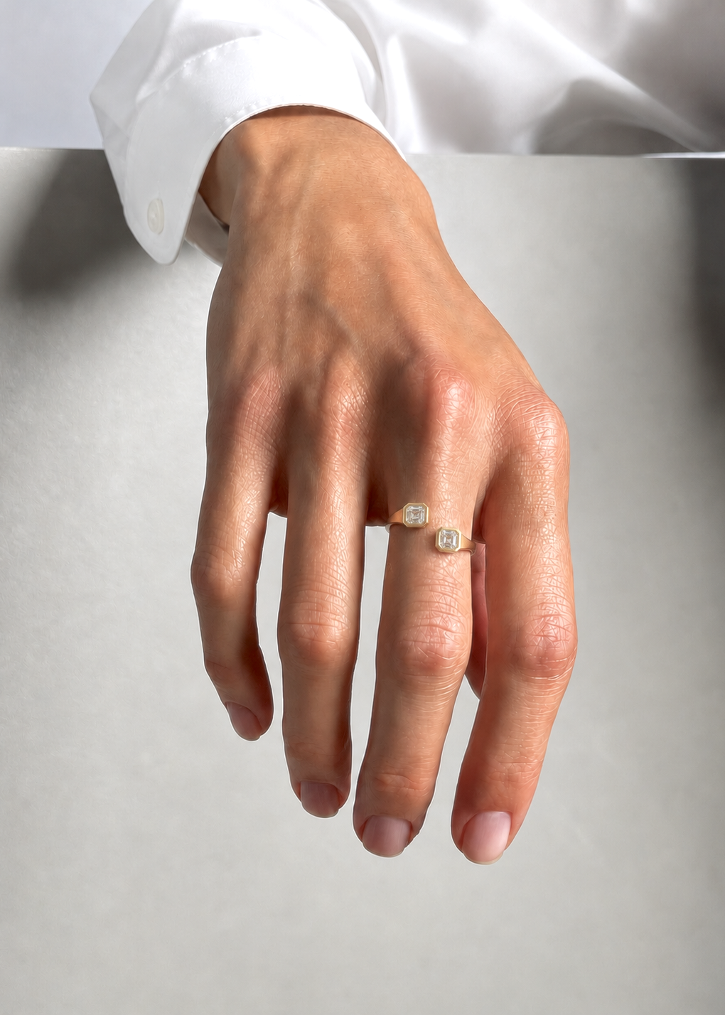 Hand wearing a gold ring with a diamond on a light gray background